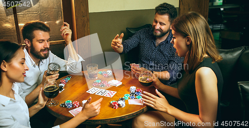 Image of Side view photo of friends sitting at wooden table. Friends having fun while playing board game.