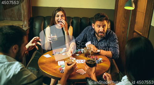 Image of Side view photo of friends sitting at wooden table. Friends having fun while playing board game.