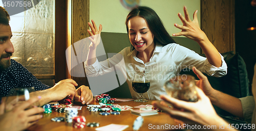 Image of Side view photo of friends sitting at wooden table. Friends having fun while playing board game.