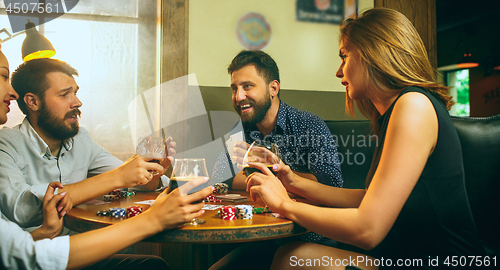 Image of Side view photo of friends sitting at wooden table. Friends having fun while playing board game.