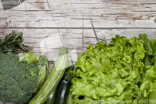 Image of Variety of green organic vegetables on rustic wooden background.