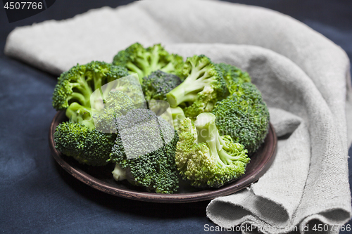 Image of Fresh green organic broccoli in brown plate and linen napkin.