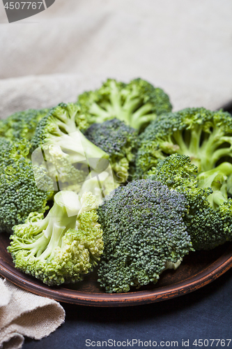 Image of Fresh green organic broccoli in brown plate and linen napkin.