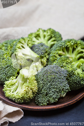 Image of Fresh green organic broccoli in brown plate and linen napkin.