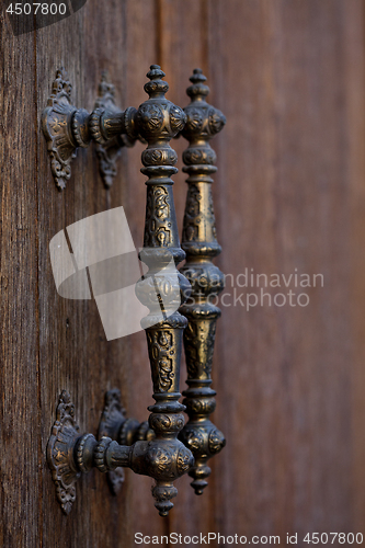 Image of Ancient Italian metal door handles on brown wooden door. 