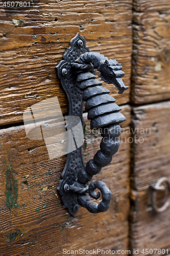 Image of Ancient Italian metal door handle on brown wooden door. 