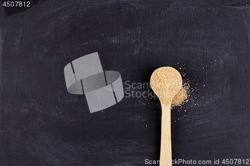 Image of Brown cane sugar in wooden spoon on black background. 