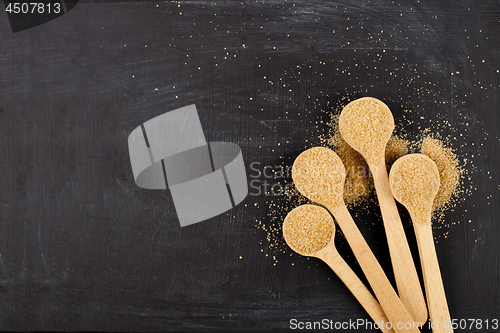 Image of Brown cane sugar in four wooden spoons on black background.