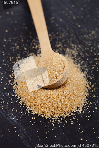 Image of Brown cane sugar in wooden spoon on black board.