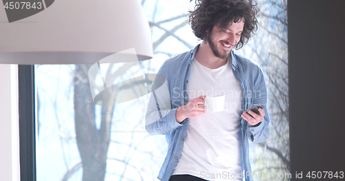 Image of young man drinking coffee and using a mobile phone  at home