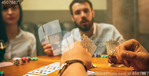 Image of Side view photo of friends sitting at wooden table. Friends having fun while playing board game.