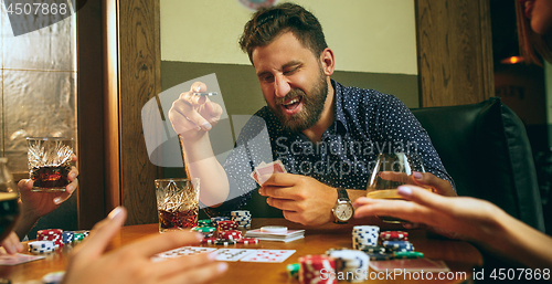 Image of Side view photo of friends sitting at wooden table. Friends having fun while playing board game.