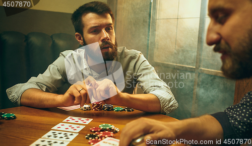 Image of Side view photo of friends sitting at wooden table. Friends having fun while playing board game.