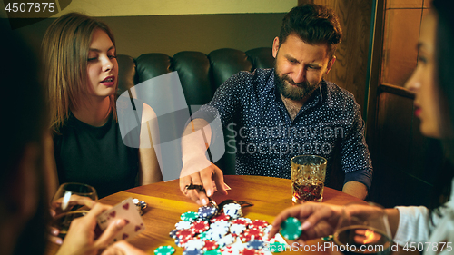 Image of Side view photo of friends sitting at wooden table. Friends having fun while playing board game.