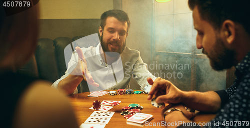 Image of Side view photo of friends sitting at wooden table. Friends having fun while playing board game.