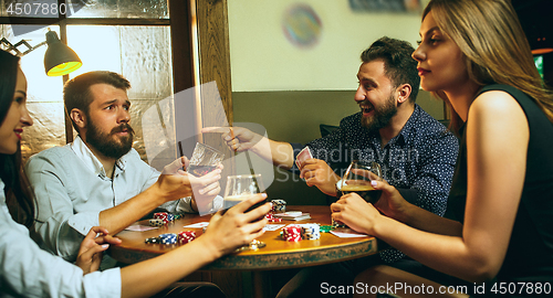 Image of Side view photo of friends sitting at wooden table. Friends having fun while playing board game.