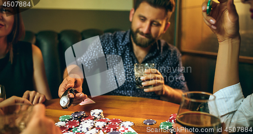 Image of Side view photo of friends sitting at wooden table. Friends having fun while playing board game.