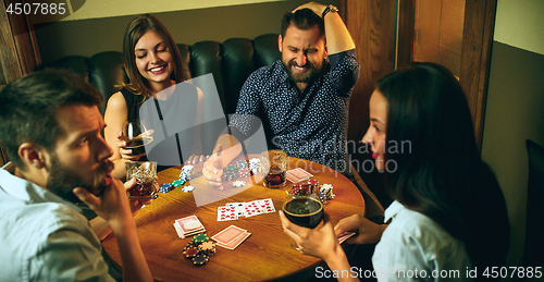 Image of Side view photo of friends sitting at wooden table. Friends having fun while playing board game.