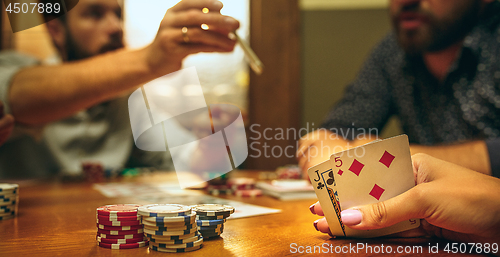 Image of Side view photo of friends sitting at wooden table. Friends having fun while playing board game.