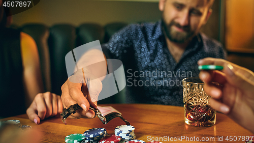 Image of Side view photo of friends sitting at wooden table. Friends having fun while playing board game.