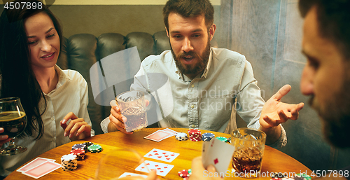 Image of Side view photo of friends sitting at wooden table. Friends having fun while playing board game.