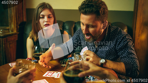Image of Friends sitting at wooden table. Friends having fun while playing board game.