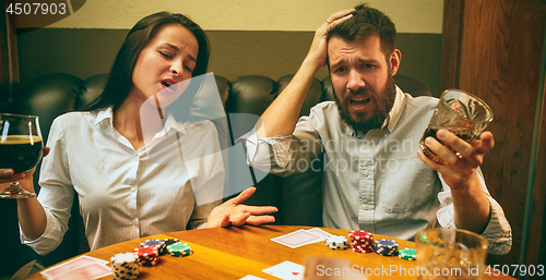 Image of Side view photo of friends sitting at wooden table. Friends having fun while playing board game.