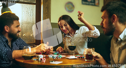 Image of Side view photo of friends sitting at wooden table. Friends having fun while playing board game.