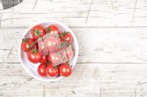 Image of Fresh tomatoes in white bowl on rustic wooden table.