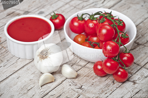 Image of Fresh tomatoes in white bowl, sauce and raw garlic on rustic woo