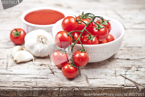 Image of Fresh tomatoes in white bowl, sauce and raw garlic on rustic woo