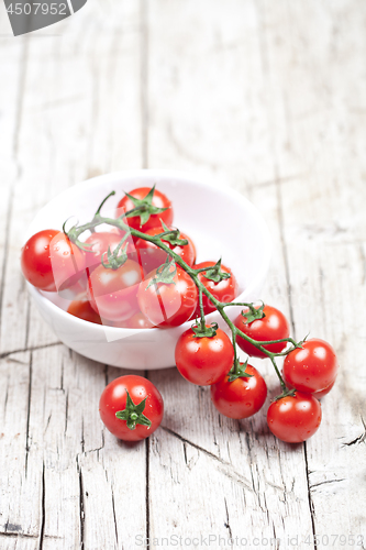 Image of Fresh tomatoes in white bowl on rustic wooden table. 