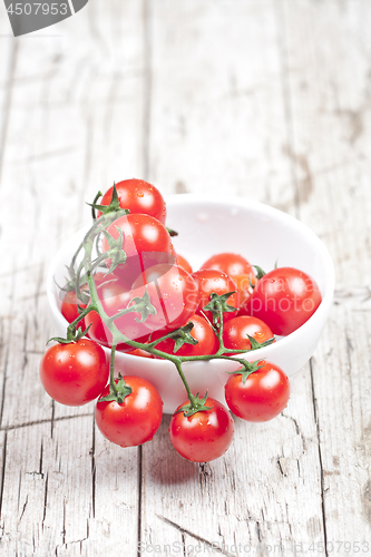 Image of Fresh tomatoes in white bowl on rustic wooden table. 