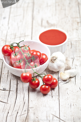 Image of Fresh tomatoes in white bowl, sauce and raw garlic on rustic woo
