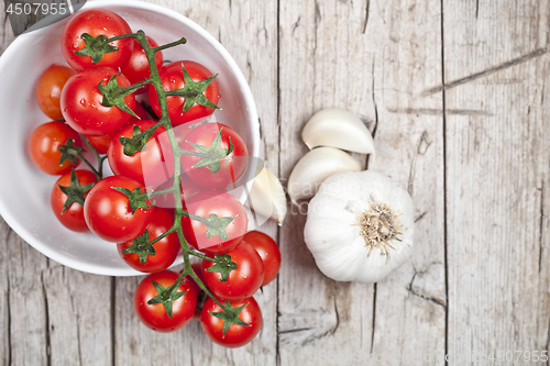 Image of Fresh tomatoes in white bowl and raw garlic on rustic wooden tab