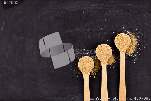 Image of Brown cane sugar in three wooden spoons on black background. 