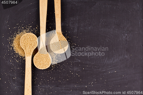 Image of Brown cane sugar in three wooden spoons on black background.