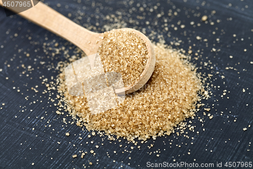 Image of Brown cane sugar in wooden spoon on black board.