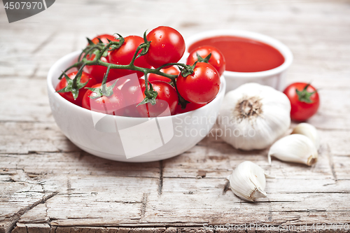 Image of Fresh tomatoes in white bowl, sauce and raw garlic on rustic woo