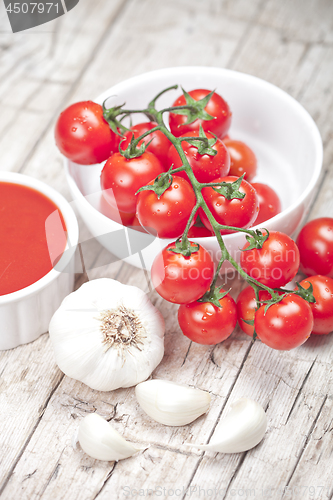 Image of Fresh tomatoes in white bowl, sauce and raw garlic on rustic woo