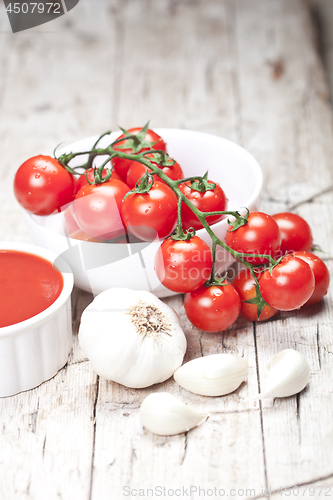 Image of Fresh tomatoes in white bowl, sauce and raw garlic on rustic woo