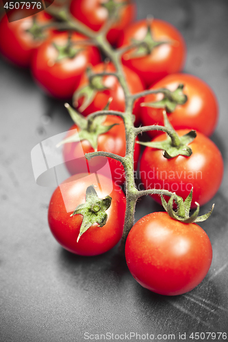 Image of Fresh organic cherry tomatoes bunch closeup on black board.