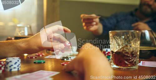 Image of Side view photo of friends sitting at wooden table. Friends having fun while playing board game.