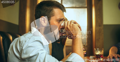 Image of Side view photo of friends sitting at wooden table. Friends having fun while playing board game.