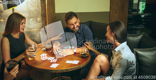 Image of Side view photo of friends sitting at wooden table. Friends having fun while playing board game.