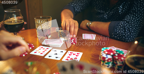 Image of Side view photo of friends sitting at wooden table. Friends having fun while playing board game.