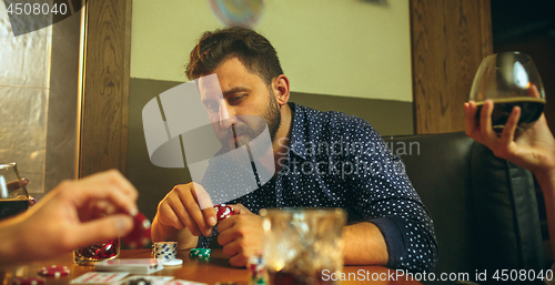 Image of Side view photo of friends sitting at wooden table. Friends having fun while playing board game.