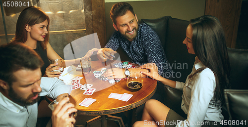 Image of Side view photo of friends sitting at wooden table. Friends having fun while playing board game.