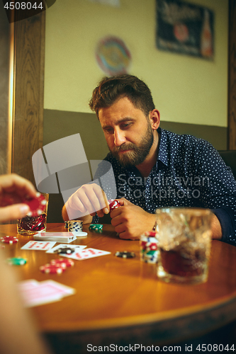 Image of Side view photo of friends sitting at wooden table. Friends having fun while playing board game.