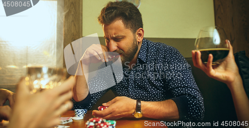 Image of Side view photo of friends sitting at wooden table. Friends having fun while playing board game.